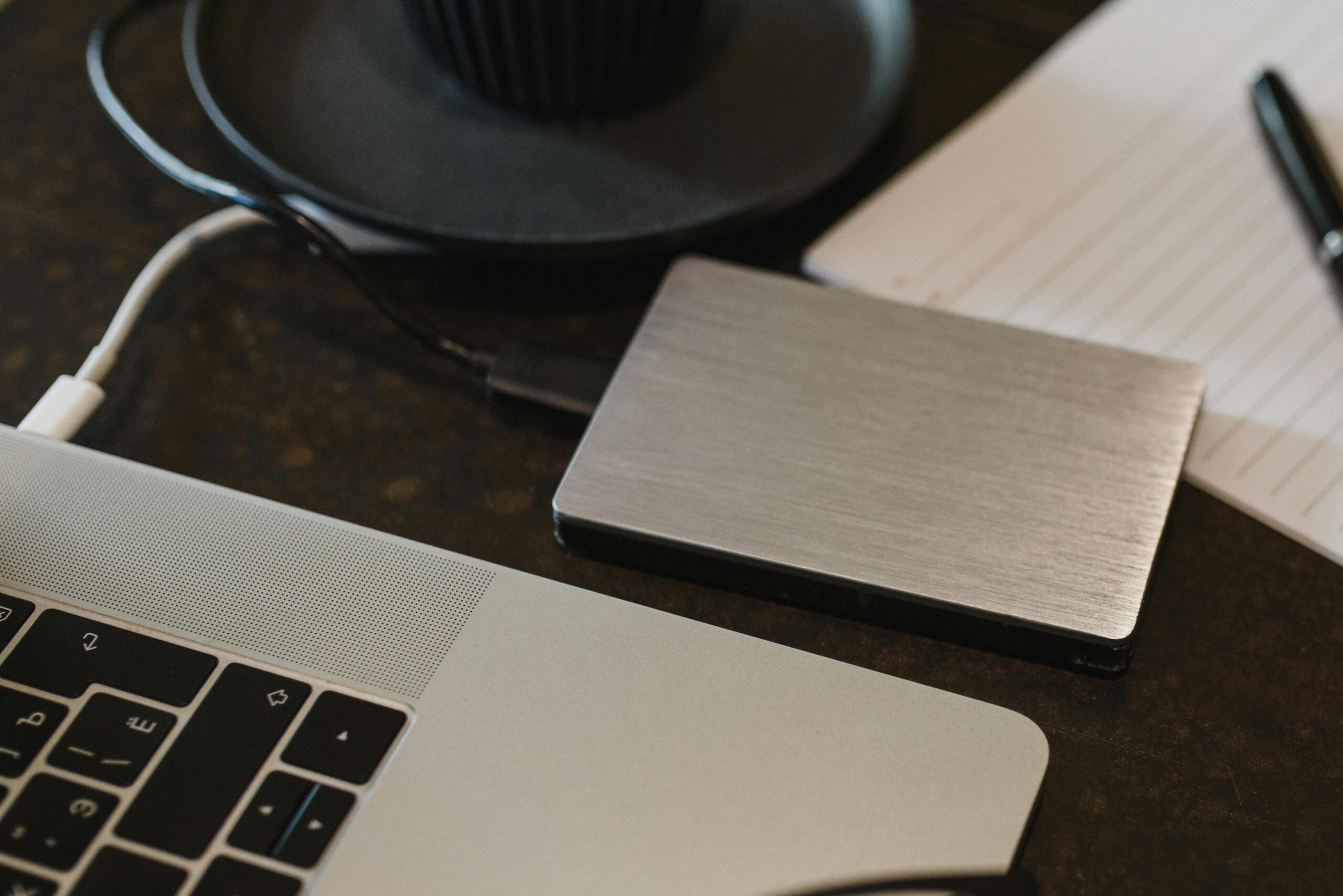 Free Closeup of an external hard drive connected to a laptop with a USB cable on a desk. Stock Photo